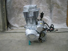 Silver motorcycle engine placed on concrete floor with neutral fabric backdrop