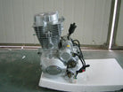 silver motorcycle engine with wiring and mounting bolts on white foam base in front of metal gate