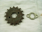 Rusty metal sprocket gear with 12 teeth and a small silver locking plate on a white fabric background