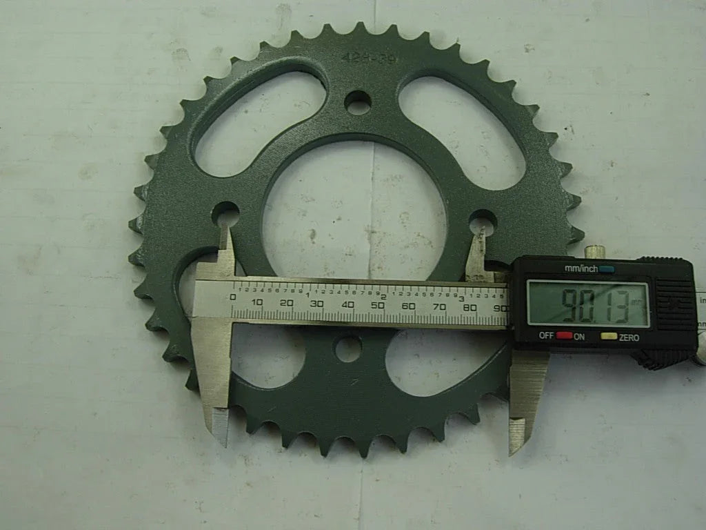 Green metal sprocket gear with digital caliper measuring 90.13 mm diameter on gray background