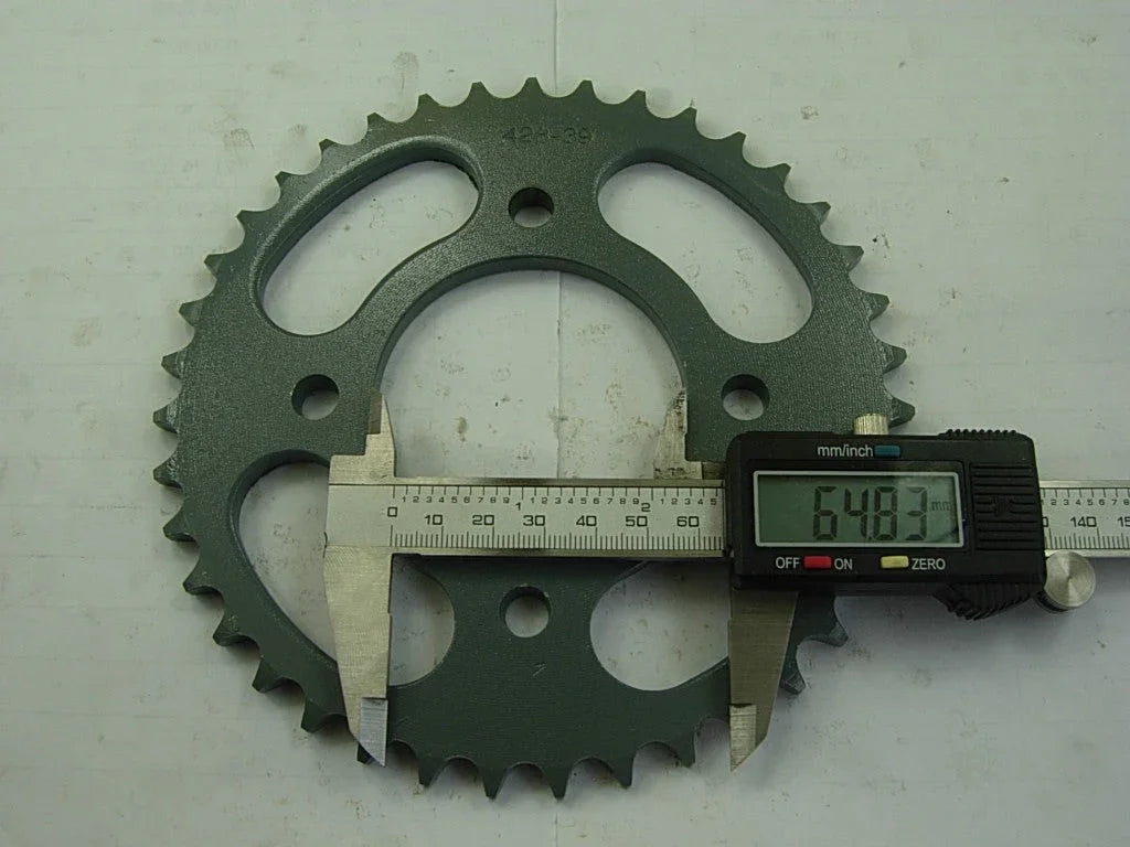 Green metal sprocket gear with digital caliper measuring 64.83 mm on white surface