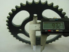 Digital caliper measuring 9.32 mm thickness of a black metal sprocket gear with teeth