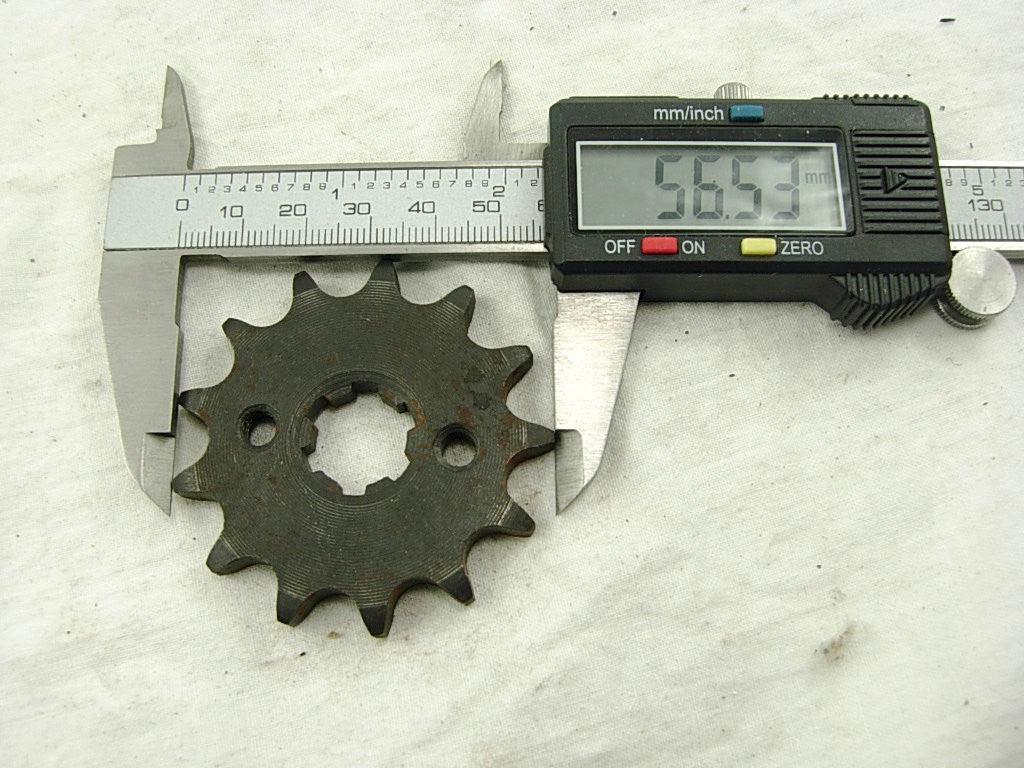 Digital caliper measuring 56.53 mm diameter of a rusty metal sprocket gear on white cloth