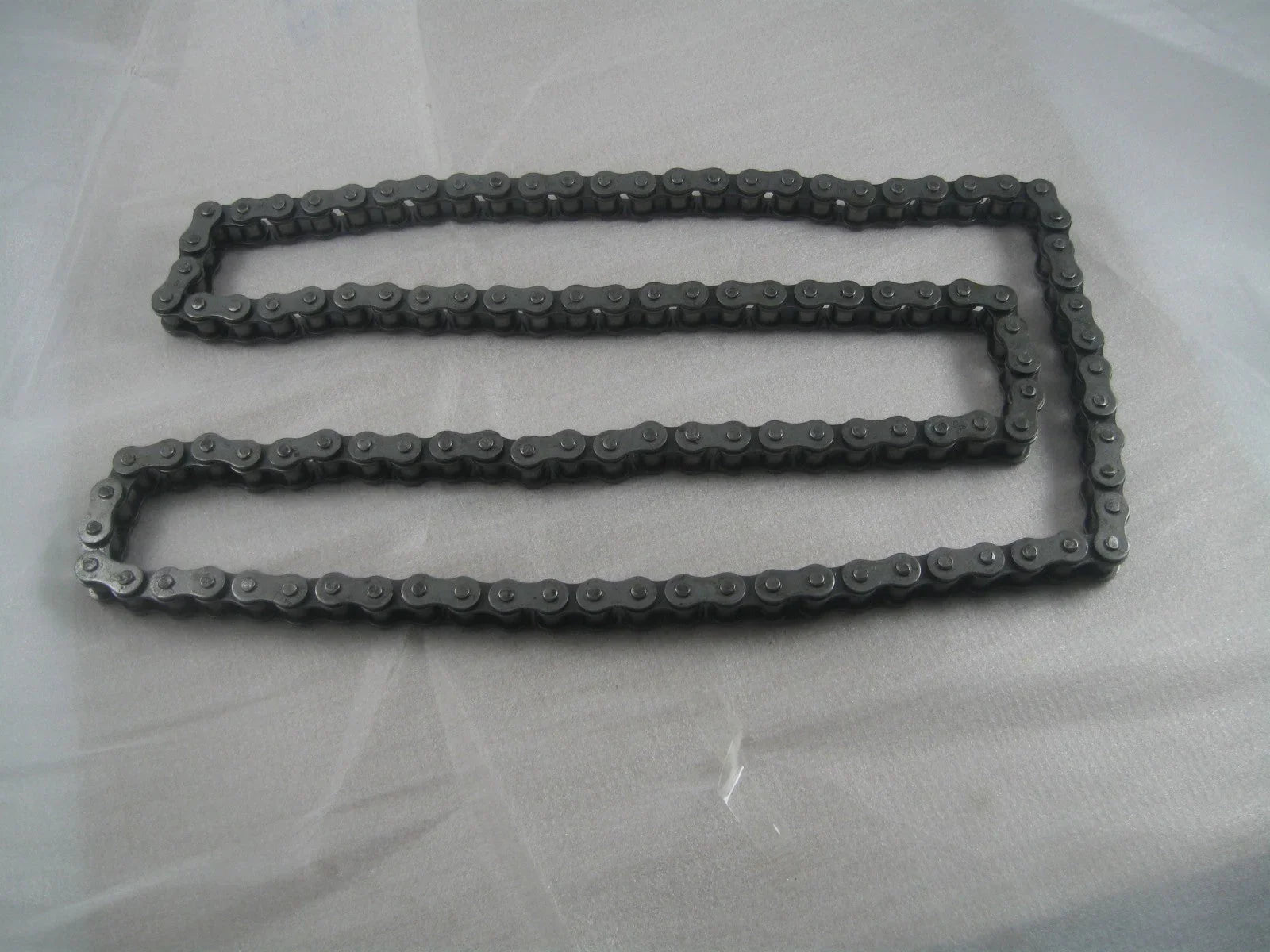 metal roller chain laid flat on light gray surface for industrial machinery