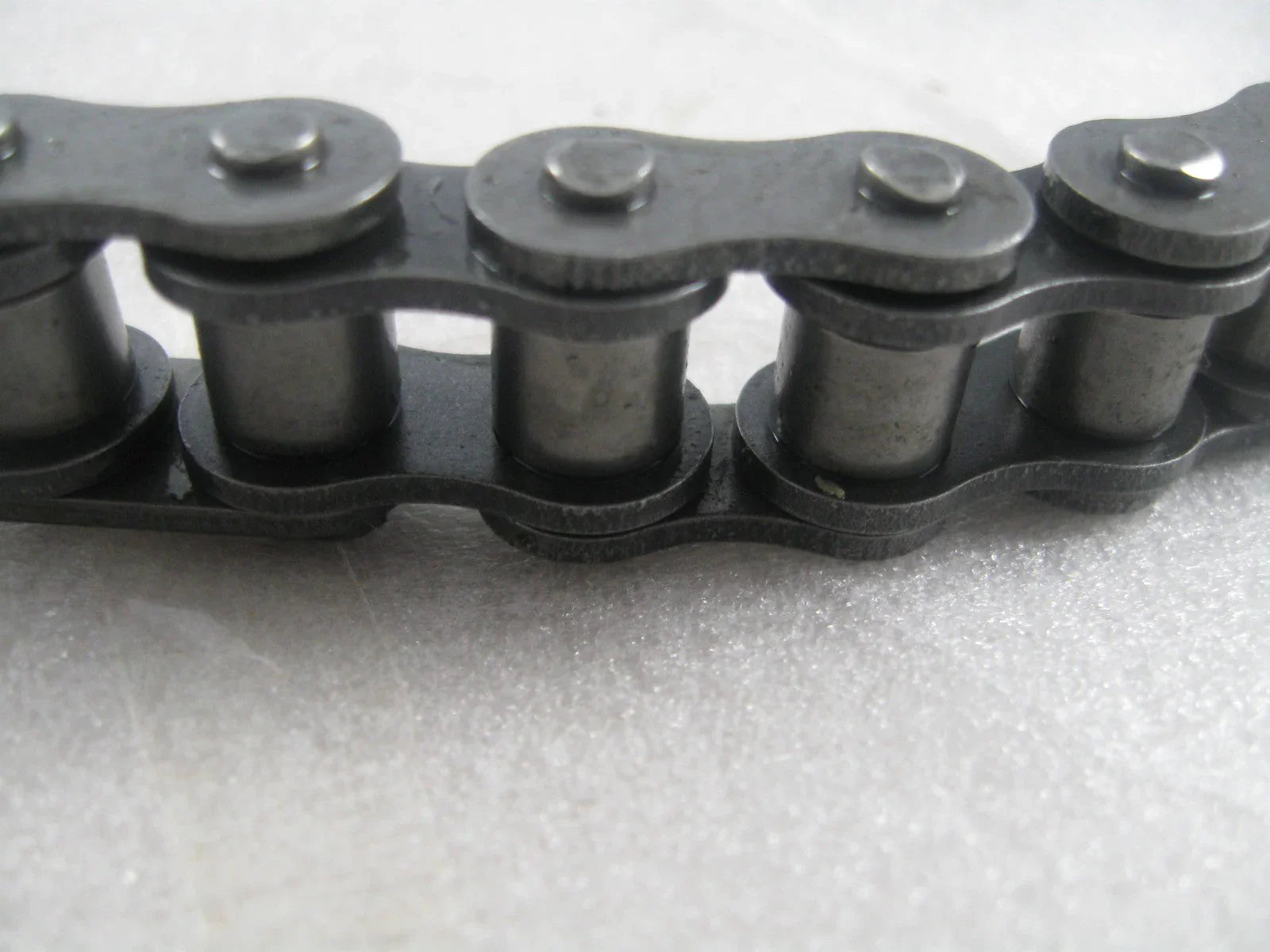 Close-up of metal roller chain links on a white textured surface