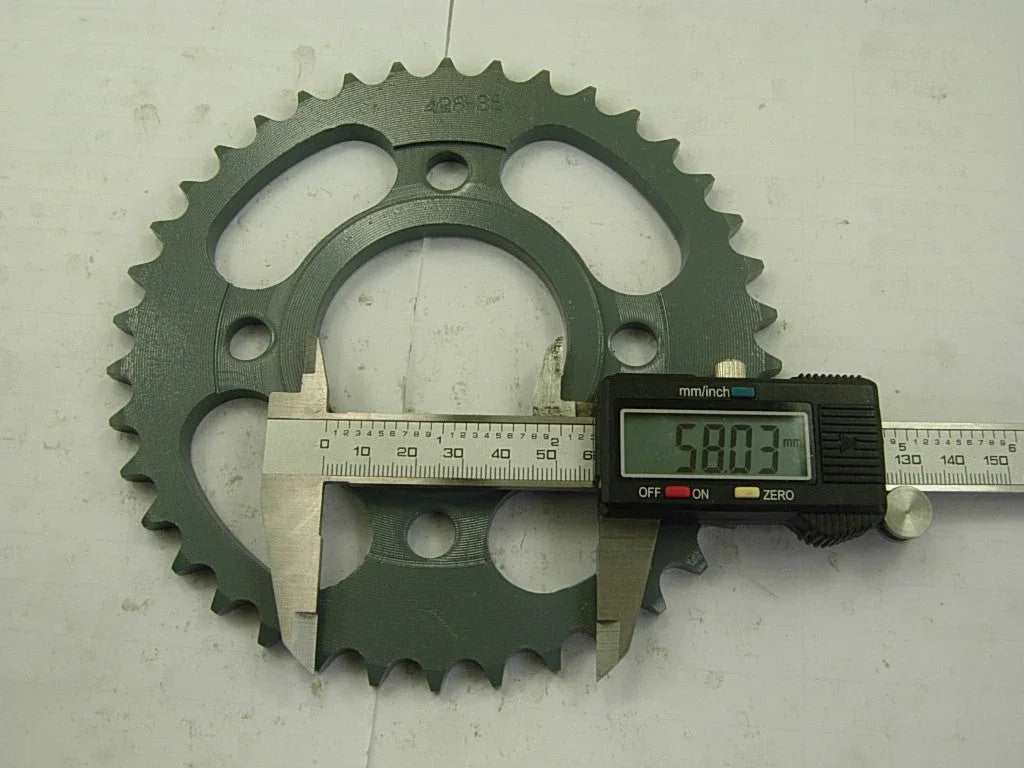 Digital caliper measuring 58.03 mm diameter of green metal sprocket on white surface