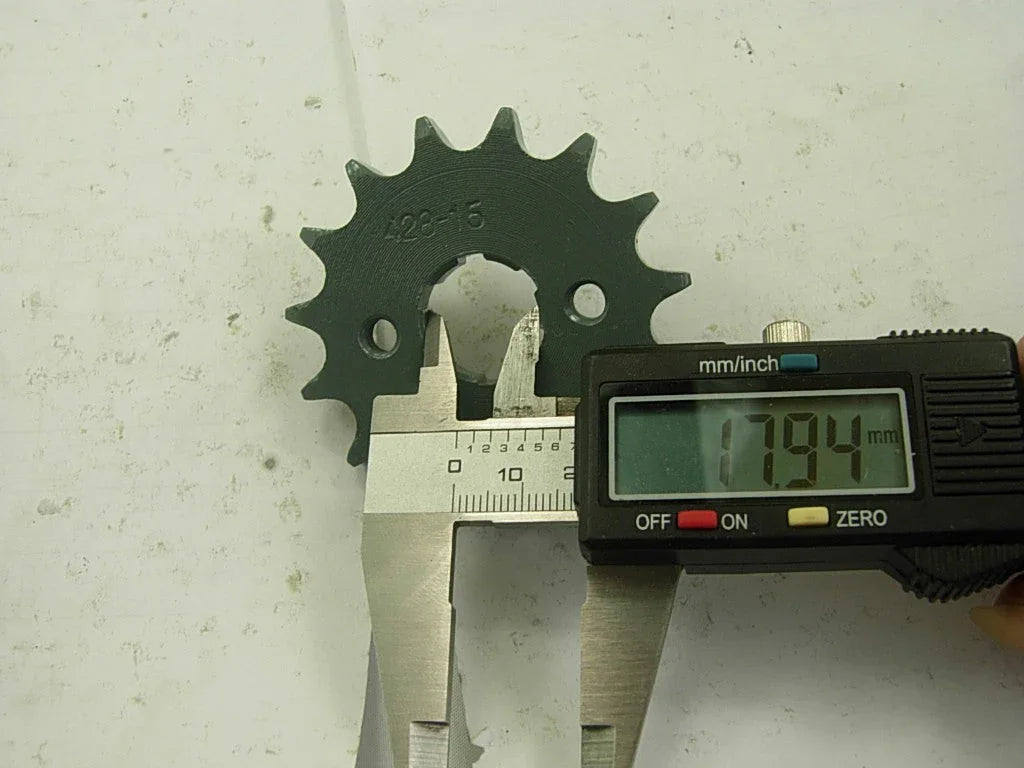 Digital caliper measuring 17.94 mm on dark gray metal sprocket gear marked 428-15