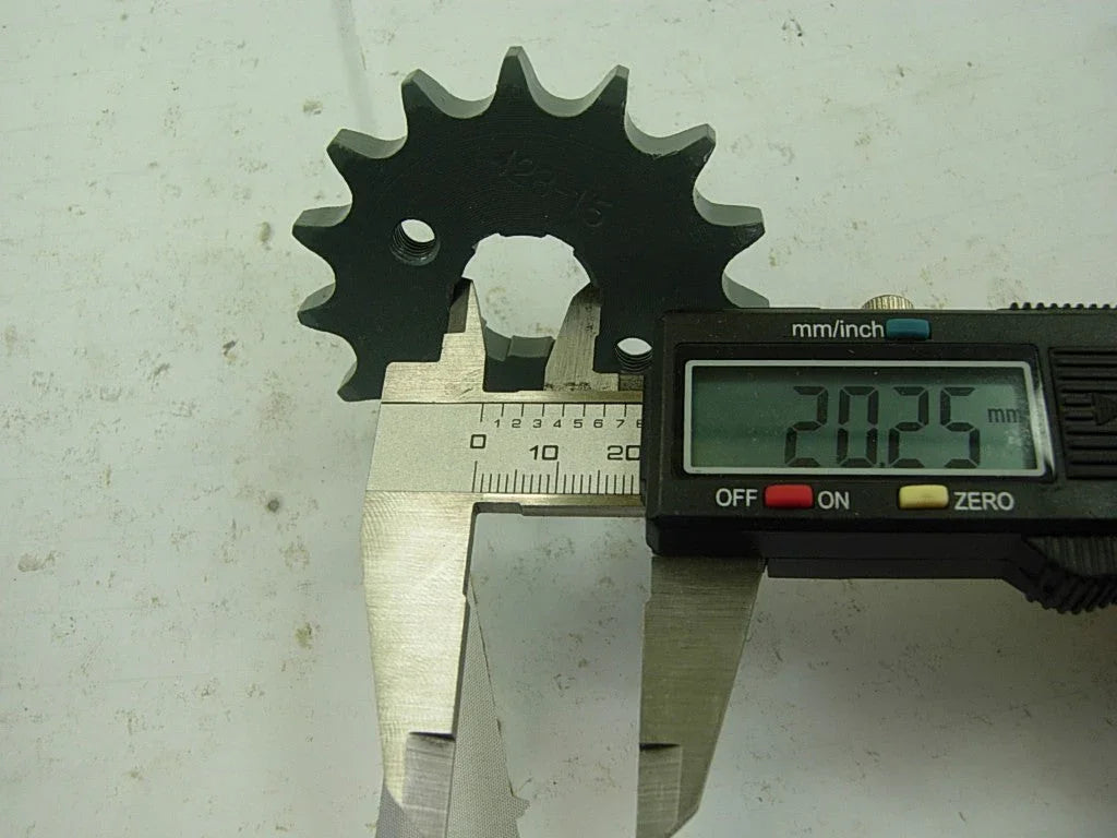 Digital caliper measuring 20.25 mm on a black metal sprocket gear with 12 teeth on white surface