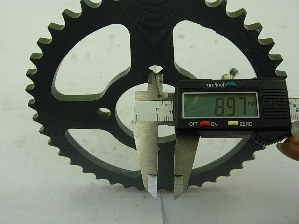 Digital caliper measuring thickness of black metal sprocket showing 8.97 mm on display
