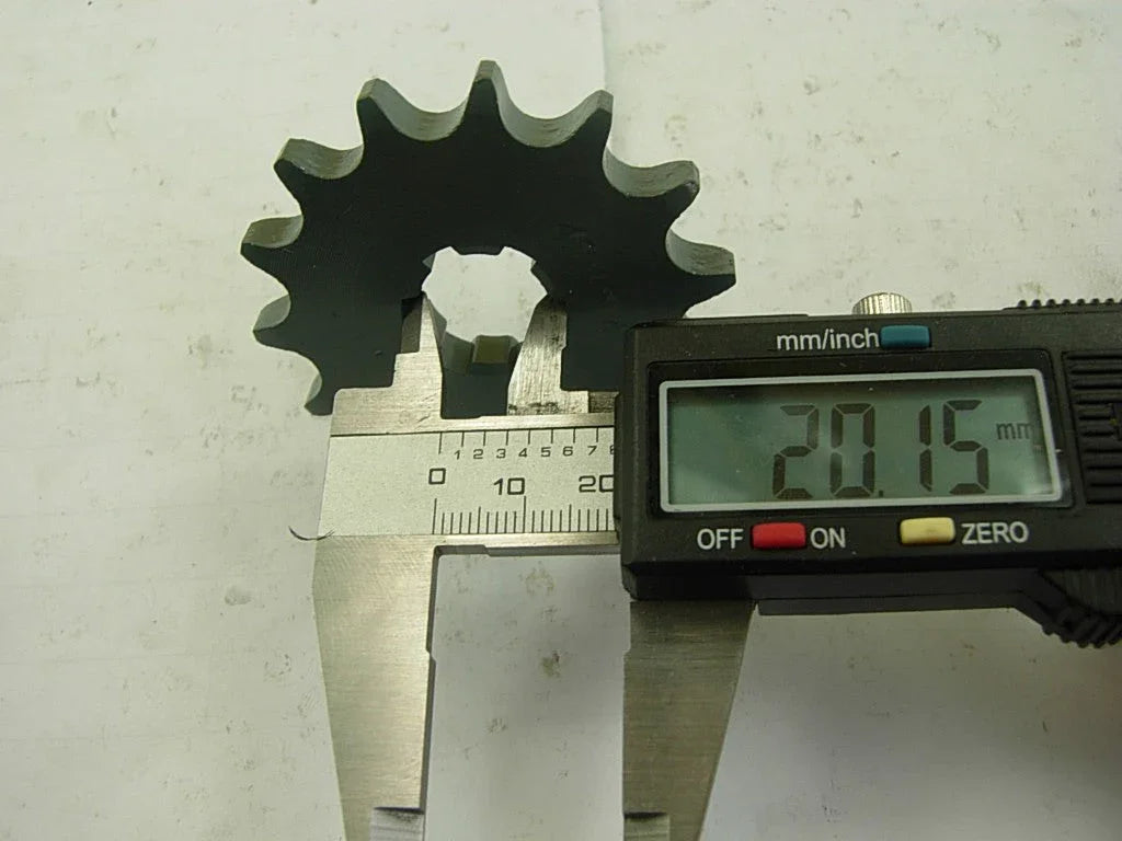 Digital caliper measuring 20.15 mm diameter of metal cogwheel gear on white surface