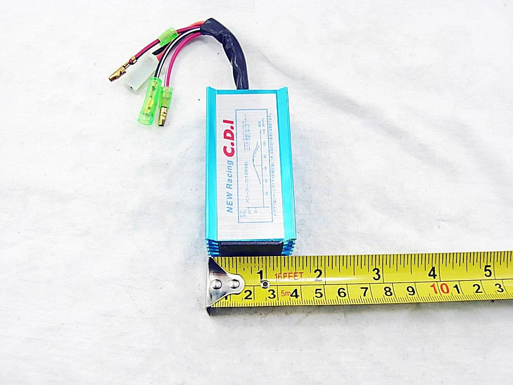 Compact blue New Racing C.D.I. unit with wiring on white background beside yellow measuring tape