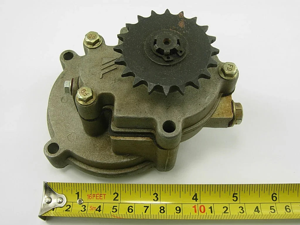 Mechanical metal gear pump with sprocket and bolts above yellow measuring tape